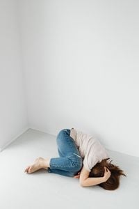 Une femme est allongée en position fœtale sur le sol d'une pièce blanche et vide, exprimant la dépression.