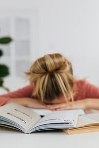 Un étudiant fatigué appuie sa tête sur la table, entouré de manuels ouverts, symbolisant la fatigue liée aux études.